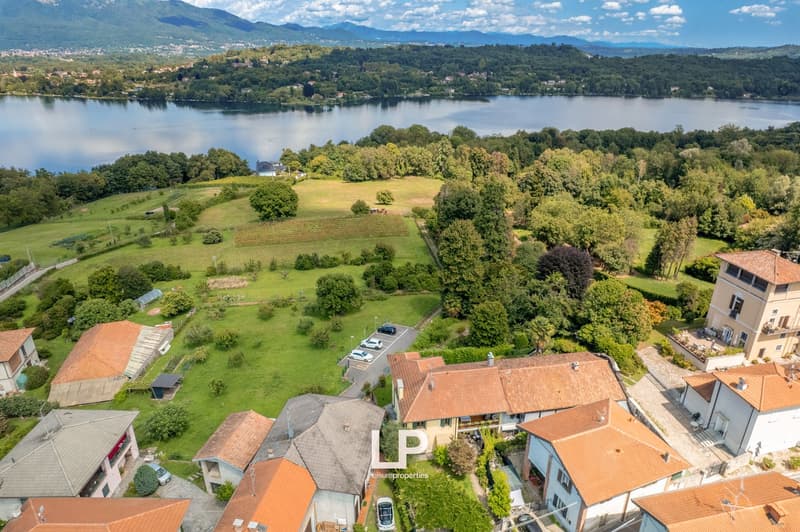 Residential area with multiple houses, some with brown roofs, surrounding a parking lot and a large field with a lake in the background.