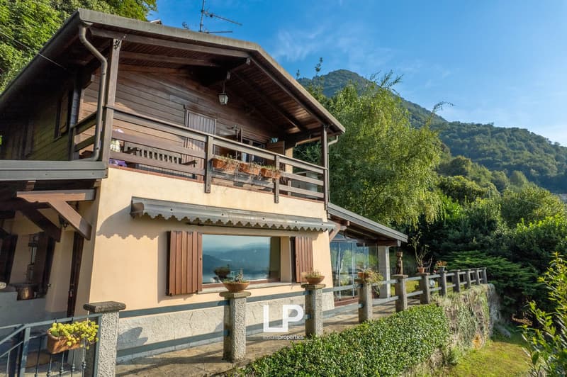 2 story house, wooden exterior, brick wall base, large windows, balcony, greenery, mountains in background