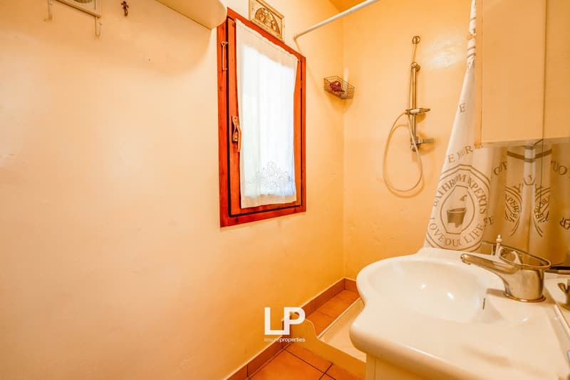 small bathroom with beige tiles, a window, a shower, a sink, and a towel rack