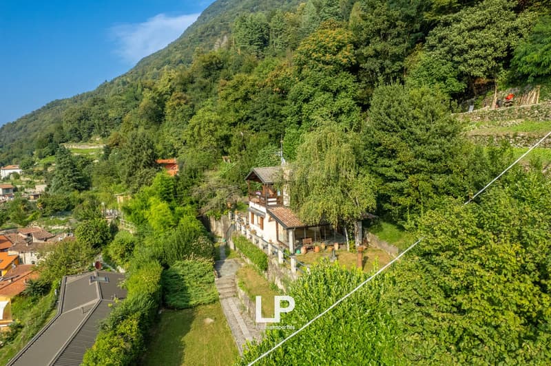 A hillside property, a small detached house, with brick-patterned roofing, nestled amidst trees and greenery, surrounded by neighboring houses on a hilly landscape. The image also includes a watermark with the text 'Leisure Properties' at the bottom right