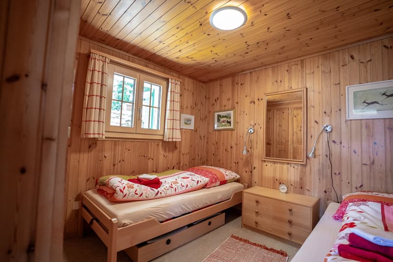 wooden bed with drawers, small cabinet, mirror, lamps, window with curtains, framed art pieces