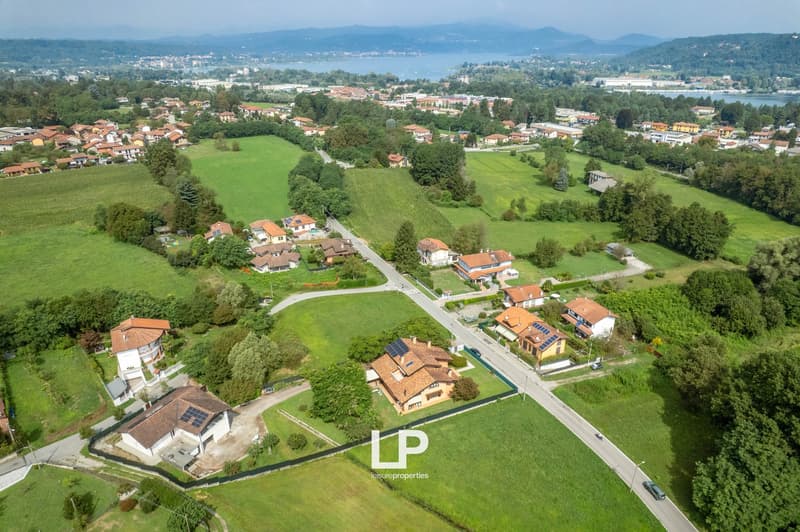 Large detached houses with tiled roofs, some with solar panels, surrounded by greenery, water body in the background, mountains in the distance.