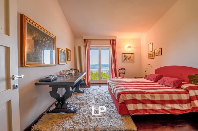 large bed with red sheets, desk, chair, large windows with view, wooden floors