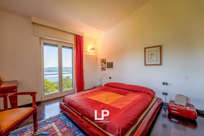 bedroom with a bed, desk, chair, rug, framed portrait on the wall, sliding glass doors with balcony view, wall lamp, power outlets
