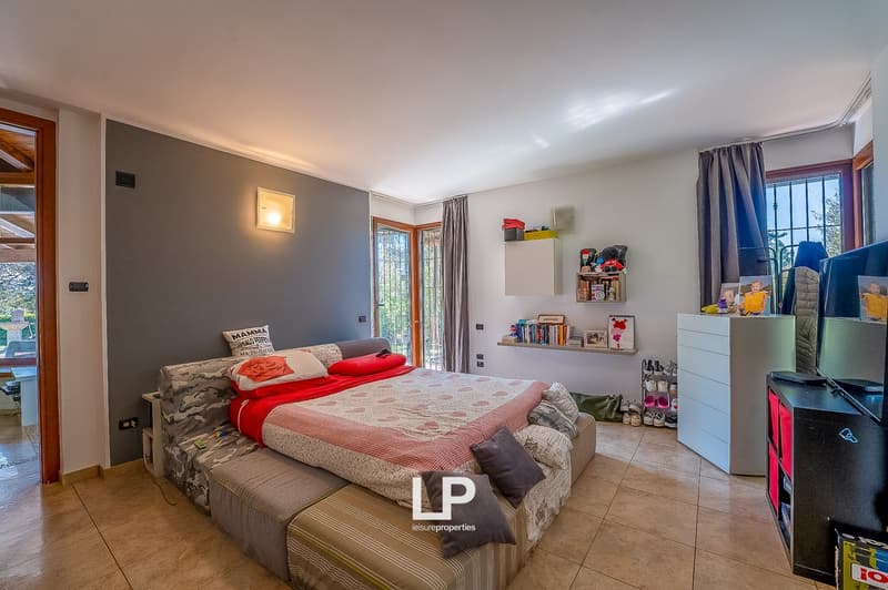 large bed with pillows, gray walls, tiled floor, shelves with books and toys, TV, wardrobe, window with curtains