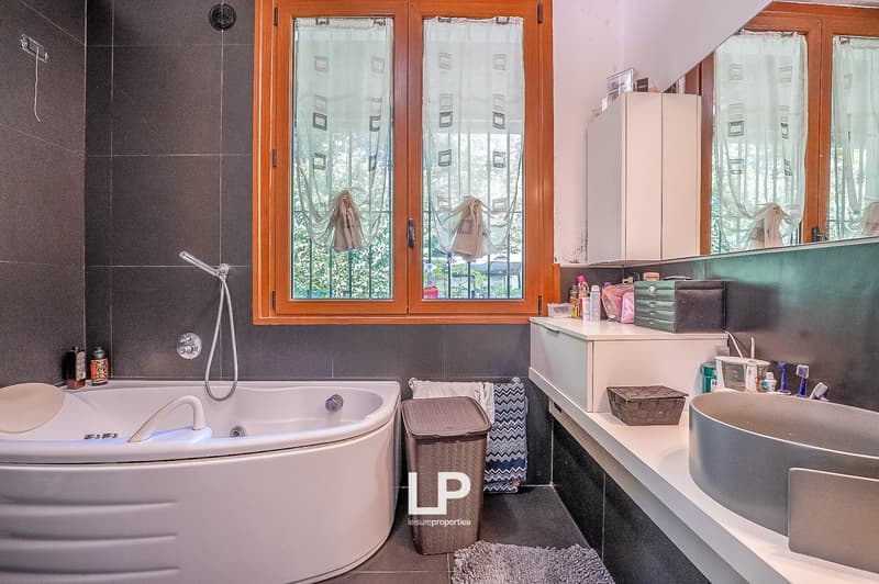 tub with shower, vanity with double sinks, mirrors, radiator, trash can