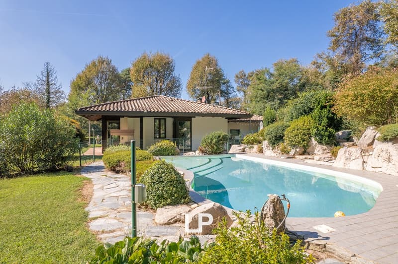single-story house with tiled roof, small swimming pool, green lawn, surrounding trees