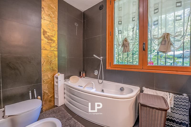 Modern bathroom with gray tiles, bathtub, toilet, sink, shelf, showerhead, and towel rack