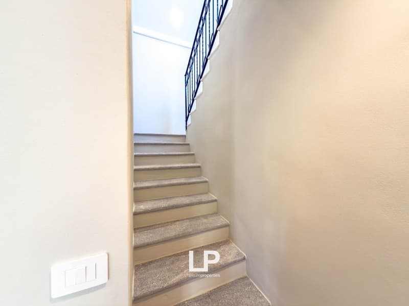 Interior image focusing on the interior staircase, black railing, gray carpeted steps, beige walls