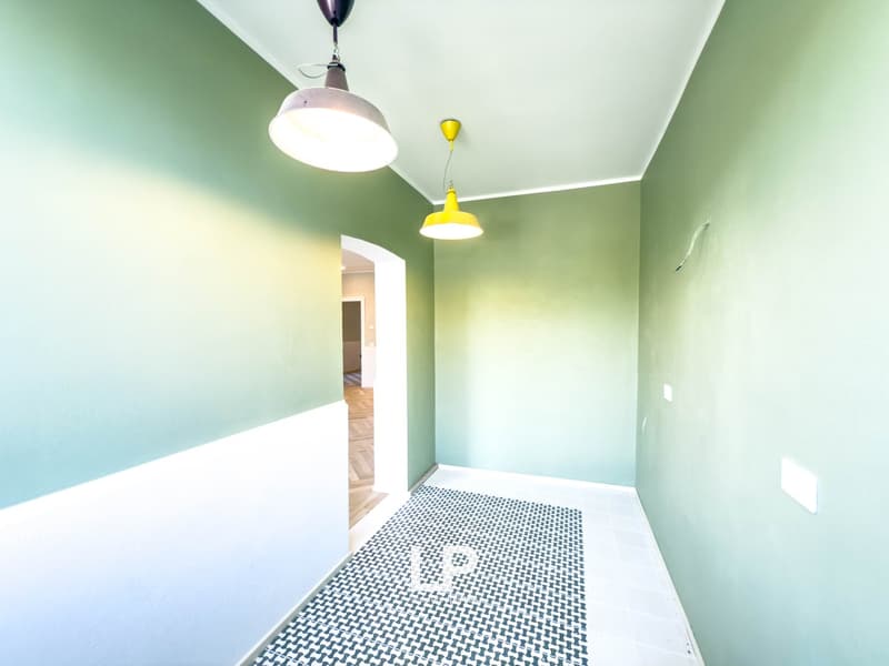 Empty hallway, with two yellow pendant lights, white and green walls, checkered floor, arch doorway