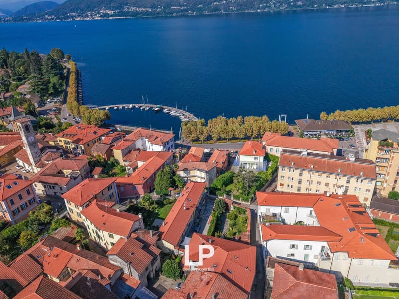 Town with multiple buildings, water body in front, red roofs, green trees