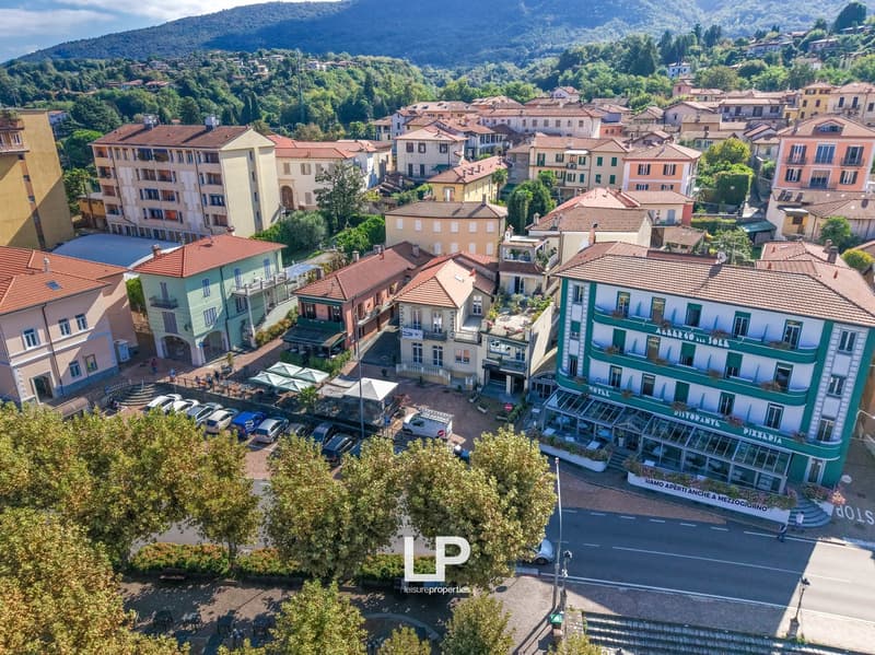 Aerial view of a small town, several buildings with terracotta roofs, parked cars, trees, mountains in the distance