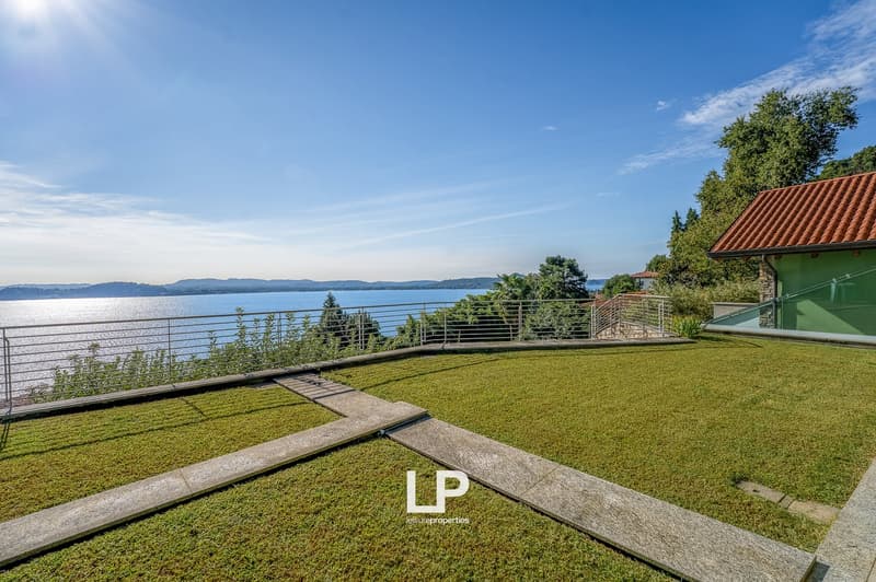 Wide green grass lawn with a steel handrail overlooking a sea view, with a red roof building in the background.