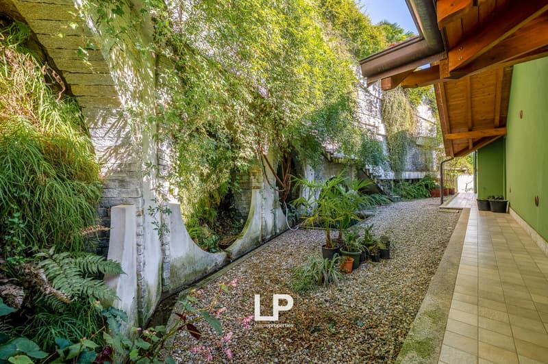 gravel path, stone walls, potted plants, greenery, covered walkway