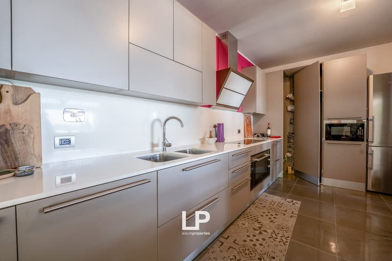 modern kitchen with stainless steel appliances, white cabinets, double sink, pink accent wall, white countertops, built-in oven and stove