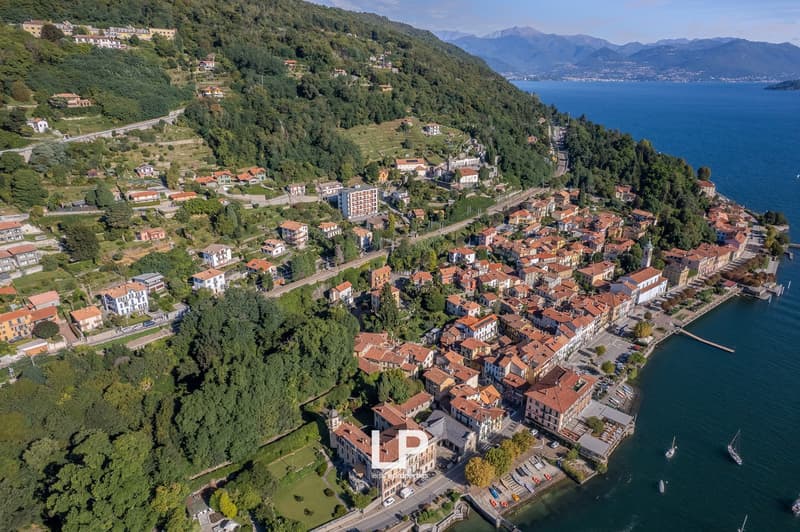Cluster of buildings on hillside, buildings on the water's edge, mountainous area, calm sea, mountains in the background, a few cars parked near the buildings