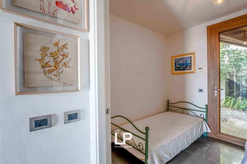 Simple bedroom with single bed, wall-mounted power outlets, framed pictures, wooden door with glass panel, tiled floor