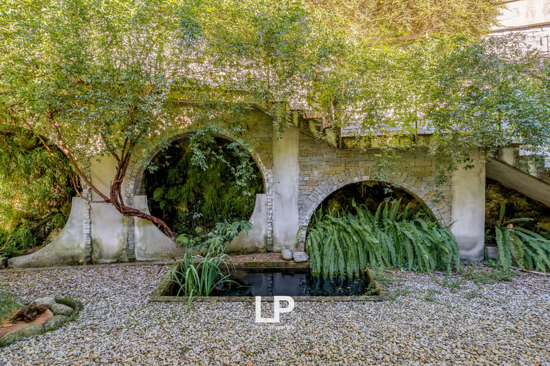 Stone pillars, arches, lush vegetation, small pond, stone pathway