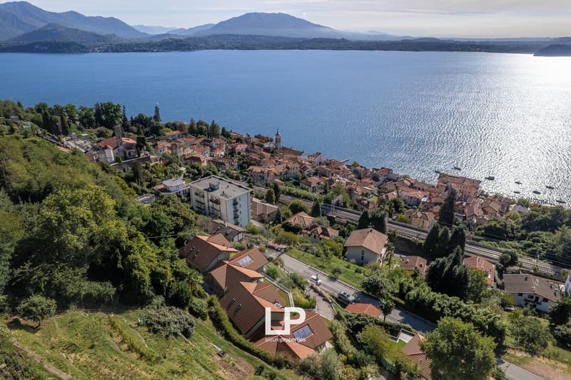 Aerial view of a hillside village with a large body of water, mountains, houses, roads, greenery, and a small path