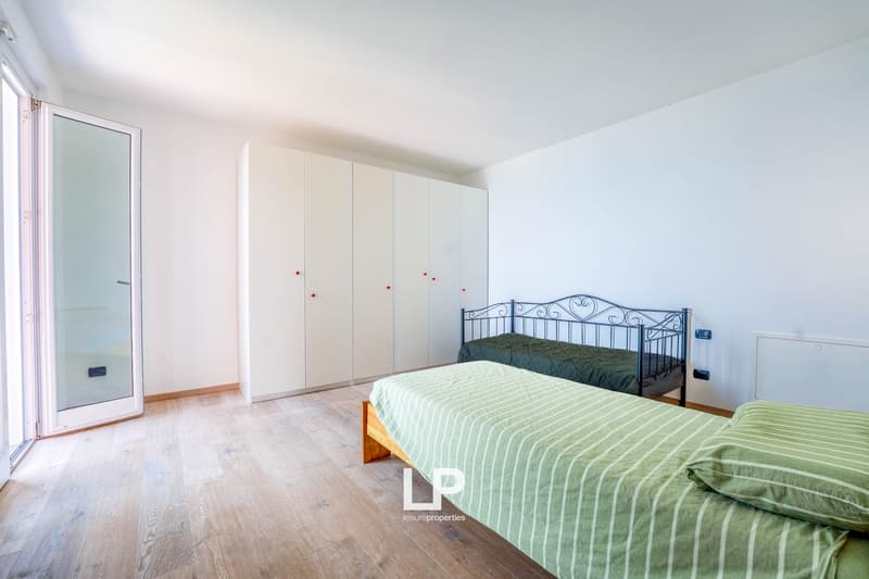 Large glass door, wooden floors, white walls, large built-in closets, two beds, green bedding and pillows, open space