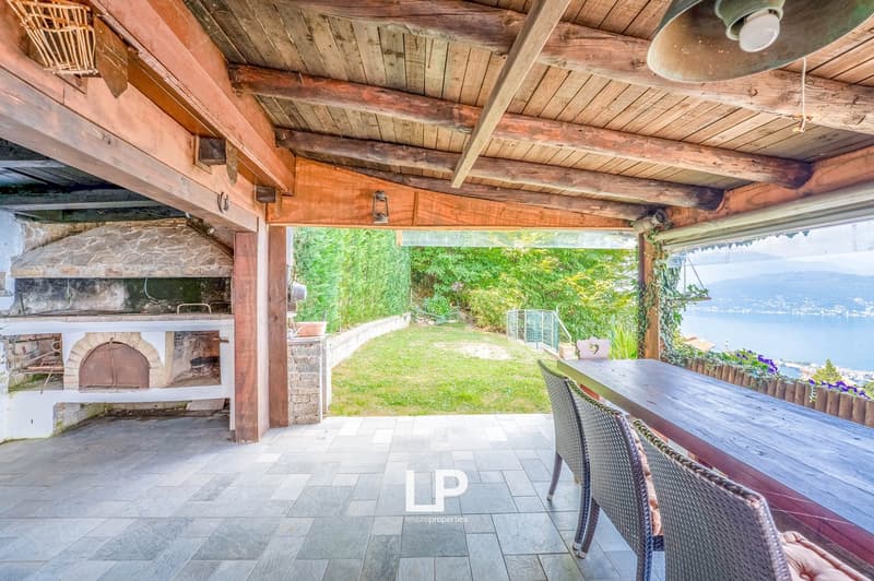 Outdoor dining area, wooden beams, brick fireplace, outdoor table, chairs, grass lawn, garden, sea view, hanging lamp