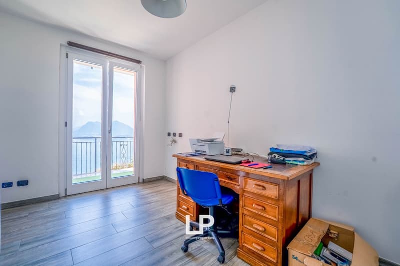 Large windows, sliding door to balcony, hardwood floor, blue chair, wooden desk, printer, view of the mountains and lake