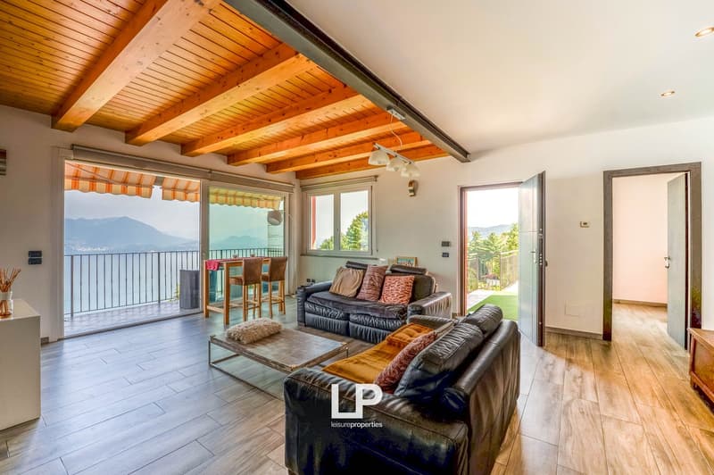 open plan layout, large living room with sofa, tables, wooden flooring, glass doors leading to balcony, modern decor, mountain view