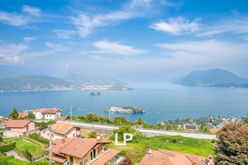 Houses with red roofs, mountainous landscape, large body of water, green hills, clear blue sky with clouds