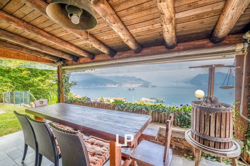 outdoor dining table, patio chairs, panoramic view of lake and mountains, wooden ceiling, bell hanging from the ceiling, grapevine press