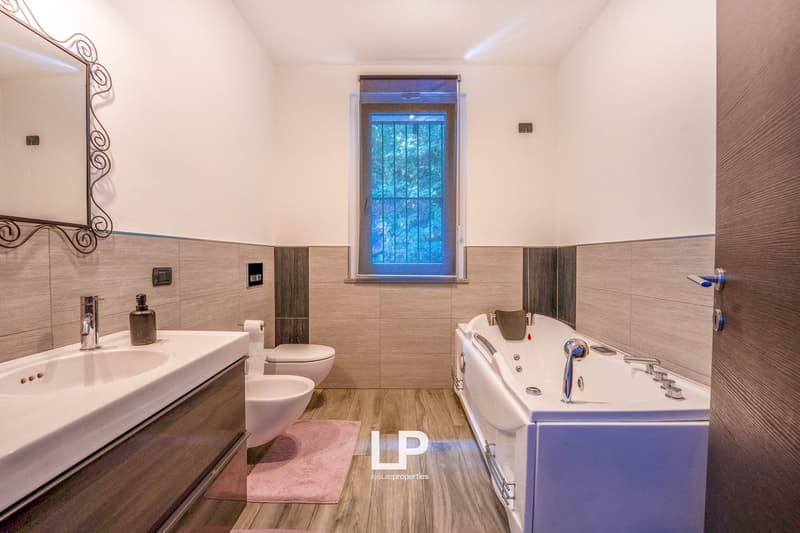 wooden floor, white walls, large mirror, modern sink, shower, bathtub, toilet, pink mat, silver faucet, decorative items, wall-mounted lights, small window