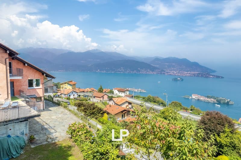 multiple houses with terracotta roofs, large body of water, mountains in the distance, balcony on the house, path leading to the houses, greenery