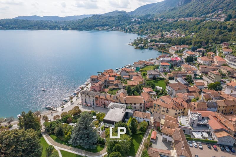 aerial view of residential area with a lake, mountains in the background, tiled rooftops, boats docked along the shore, green foliage