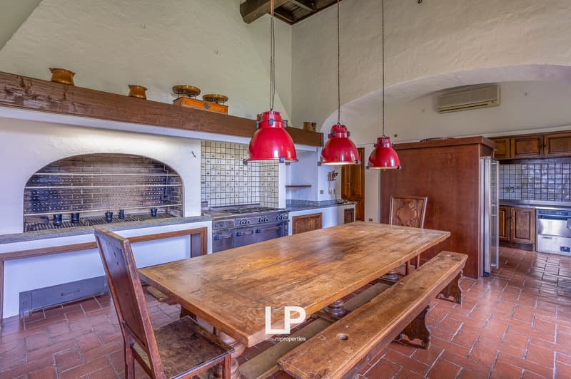 a rustic dining area with a large wooden table, wooden benches, wooden chairs, exposed brick fireplace, tiled backsplash, red pendant lights, wooden shelves, wooden cabinets, gas stove, gas oven, refrigerator, and a window