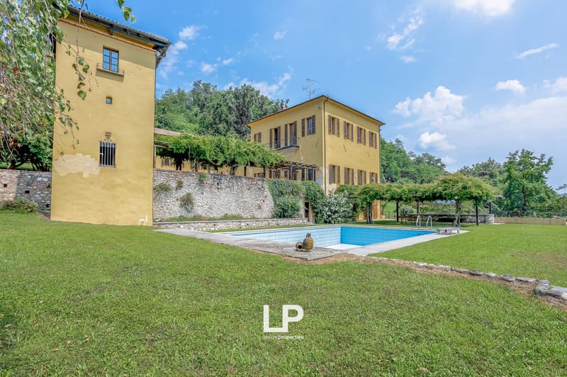 Villa, swimming pool, yellow exterior, grassy lawn, large stone wall, trees in the background
