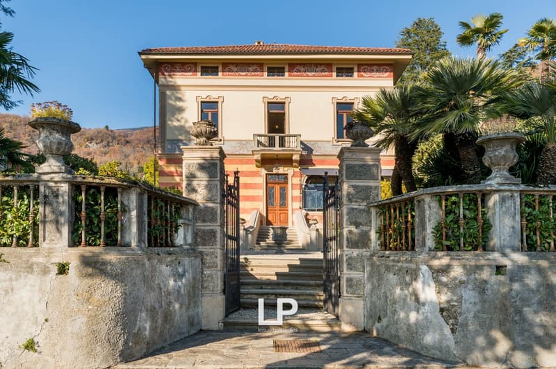 2 story house, brick walls, arched windows, large wooden door, staircases, concrete gate, trees