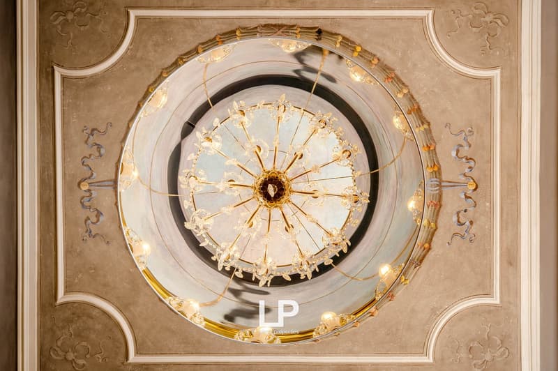 Ornate ceiling with a central crystal chandelier, decorative floral patterns, smooth painted walls.