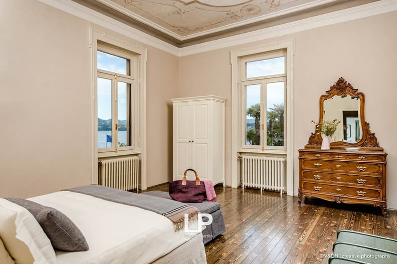 elegant room with wooden floor, radiators, bed, white sheets, blanket, pillows, nightstand, flower vase, mirror, cabinet, windows