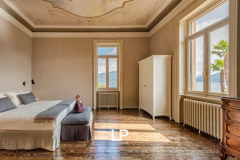 Wooden bed, grey pillows, bedspread, wardrobe, radiators, two windows with view