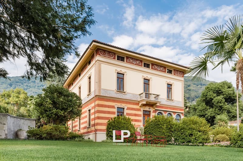 two-story red brick house, beige and red paint, arched windows, balcony, garden, lawn, mountains in the background