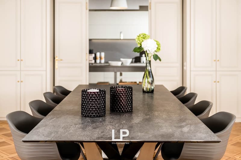 Dining table with 8 chairs, 2 candle holders, vase with flowers, parquet floor, white cabinets