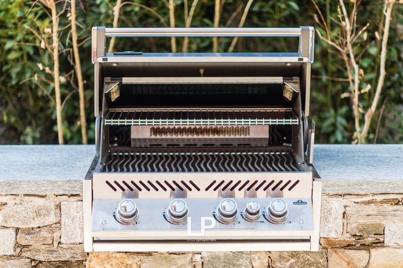 Outdoor stainless steel gas grill placed on top of a stone wall with multiple knobs for temperature control