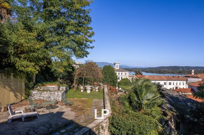 Large garden with grass, stone walls, chairs, and a table, with a river and buildings in the background.