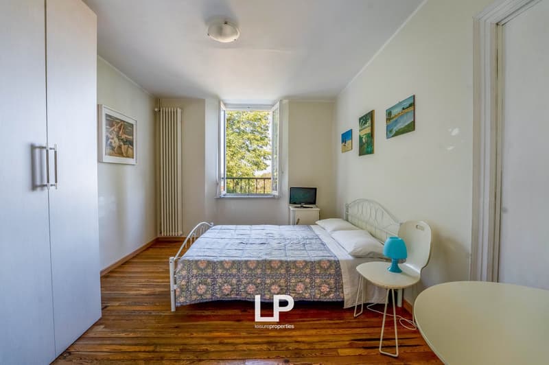 bedroom with bed, bedside table, chair, wardrobe, radiator, lamp, open window with balcony