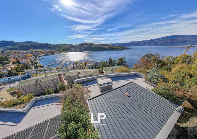 Aerial view of modern buildings, rooftops with green spaces, solar panels, mountains, and a lake in the distance