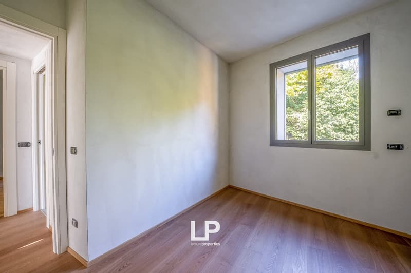 Empty room with wooden floors, white walls, and a window with a view of trees outside