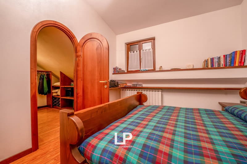 Plaid bed, wooden furniture, wooden closet, shelves with books and decor, wooden door, wooden flooring