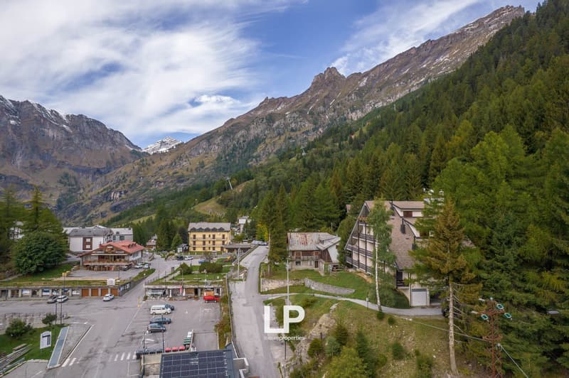 Mountainous town, multiple buildings, cars parked, road, greenery, solar panels