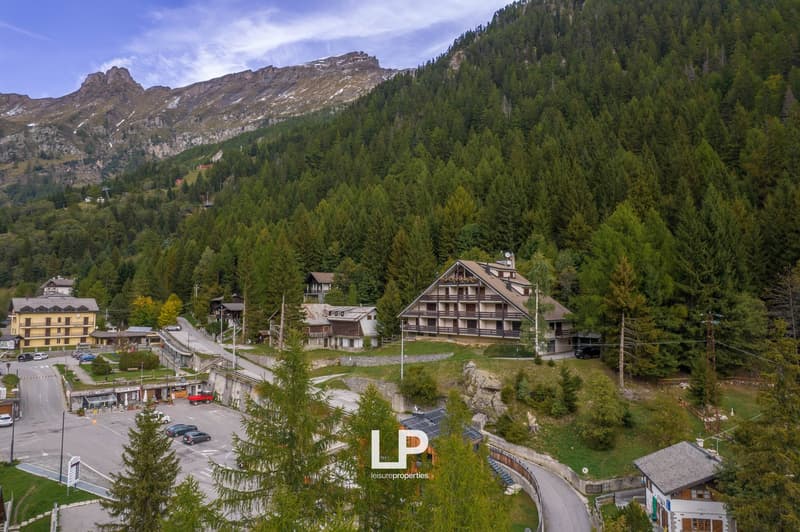 Mountainous area with several buildings, large road, parking lot with multiple cars, large trees