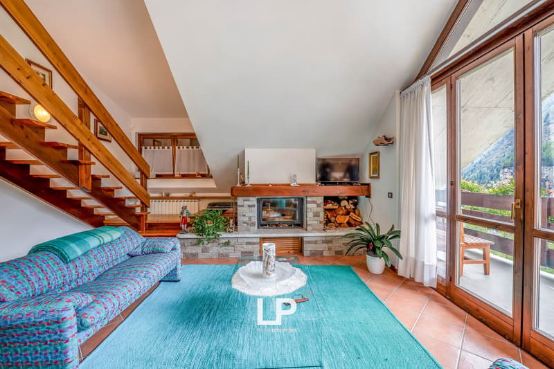 living room with fireplace, carpet, couch, wooden stairs, windows, wooden doors, balcony, wooden table, plants