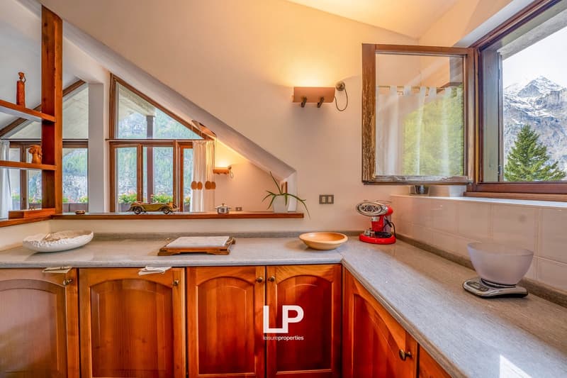 wooden cabinets, marble countertops, 2 windows, 2 small windows with mountain views, red kitchen appliance, green plant